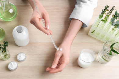 Photo of Woman applying natural cream onto hand in cosmetic laboratory, above view