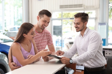 Salesman consulting young couple in car salon