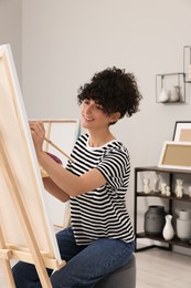 Photo of Young woman painting on easel with canvas in studio