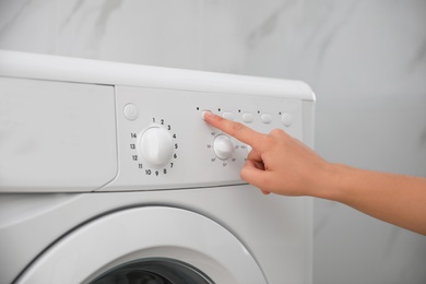 Photo of Woman pressing button on washing machine in bathroom, closeup