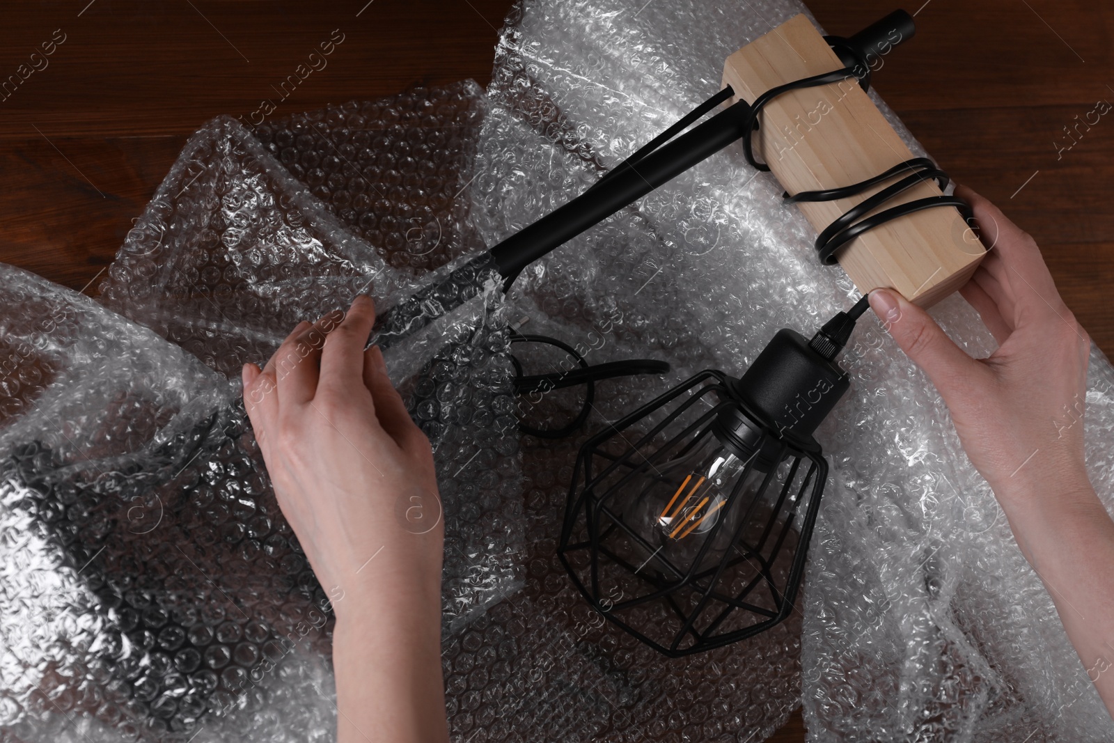 Photo of Woman covering lamp with bubble wrap at wooden table, closeup