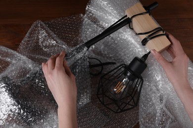 Photo of Woman covering lamp with bubble wrap at wooden table, closeup