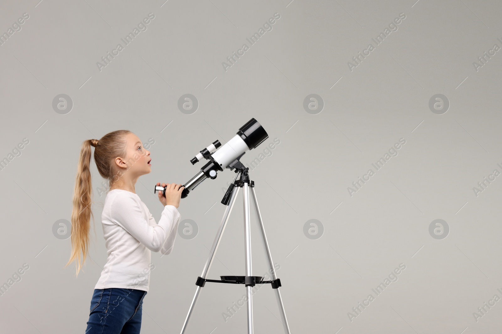 Photo of Excited little girl with telescope on light grey background, space for text