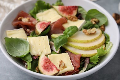 Photo of Tasty salad with brie cheese, prosciutto, pear and figs on grey table, closeup