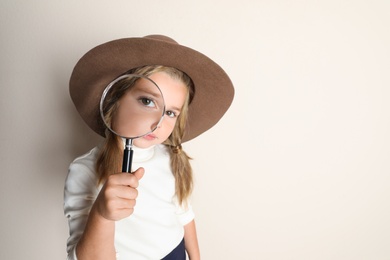 Cute little child in hat with magnifying glass playing detective on beige background, space for text