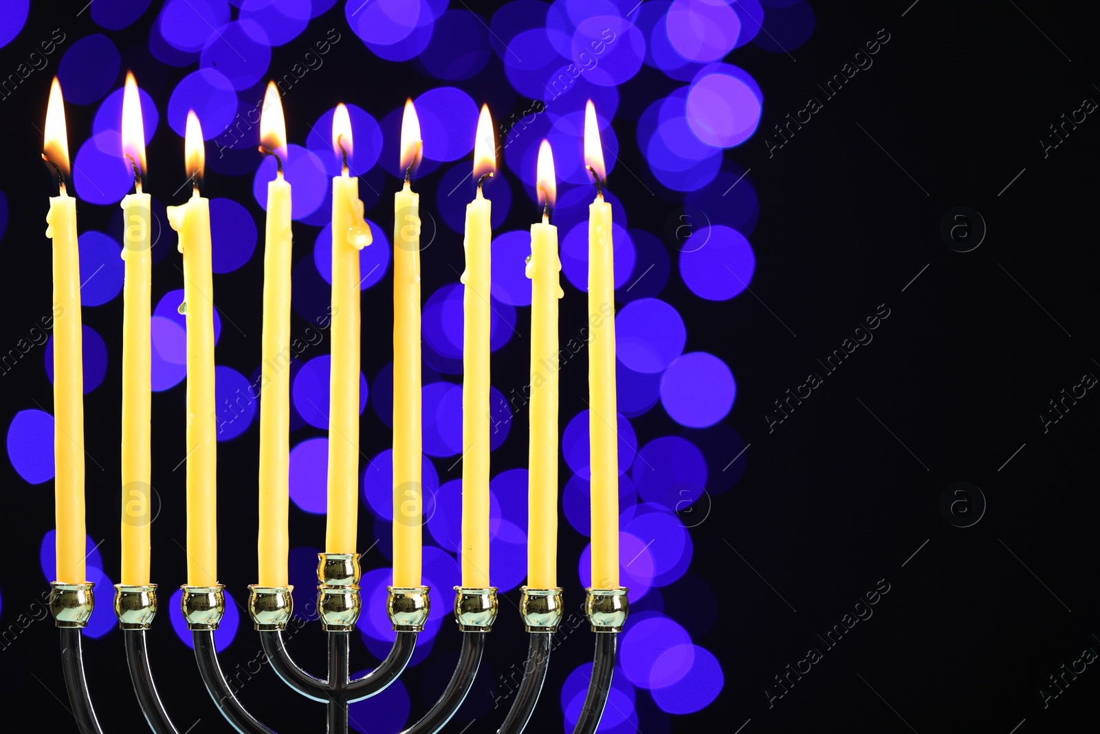 Photo of Hanukkah celebration. Menorah with burning candles against dark background with blurred lights, space for text