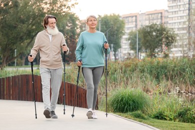 Senior man and woman performing Nordic walking outdoors, space for text