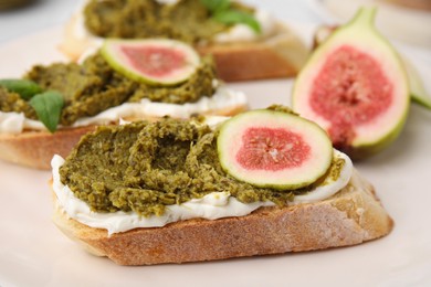 Photo of Tasty bruschettas with cream cheese, pesto sauce and figs on plate, closeup