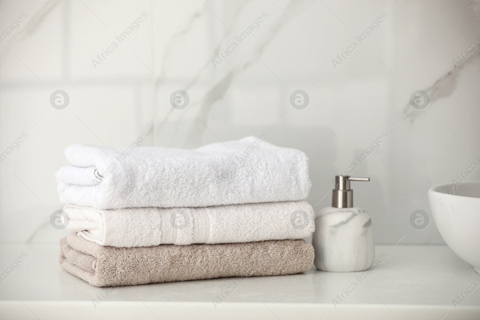 Photo of Stack of fresh towels and soap dispenser on countertop in bathroom