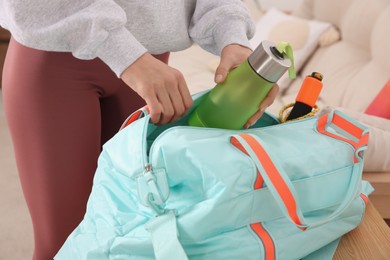 Photo of Woman packing sports stuff for training into bag at home, closeup