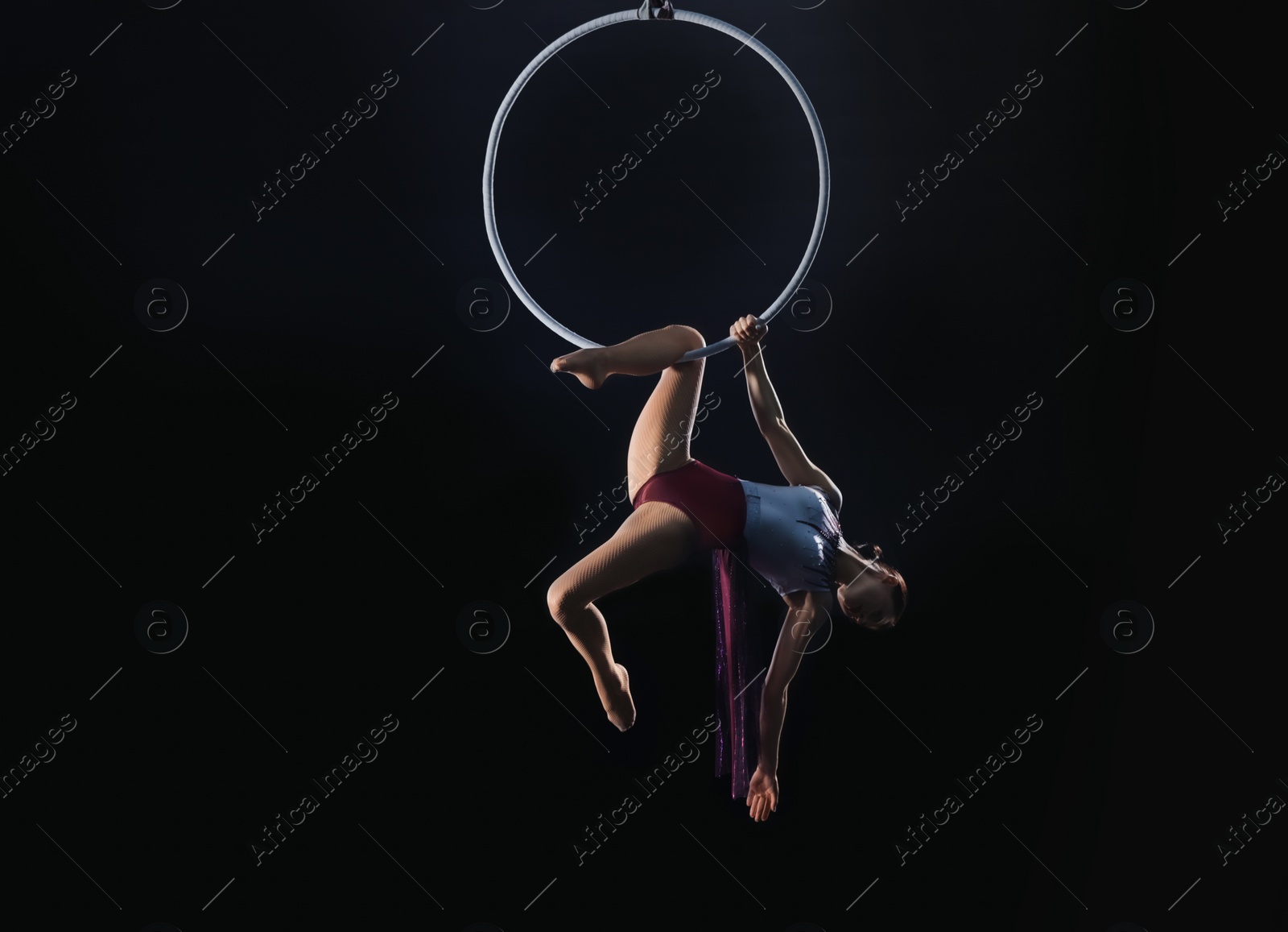 Photo of Young woman performing acrobatic element on aerial ring against dark background. Space for text