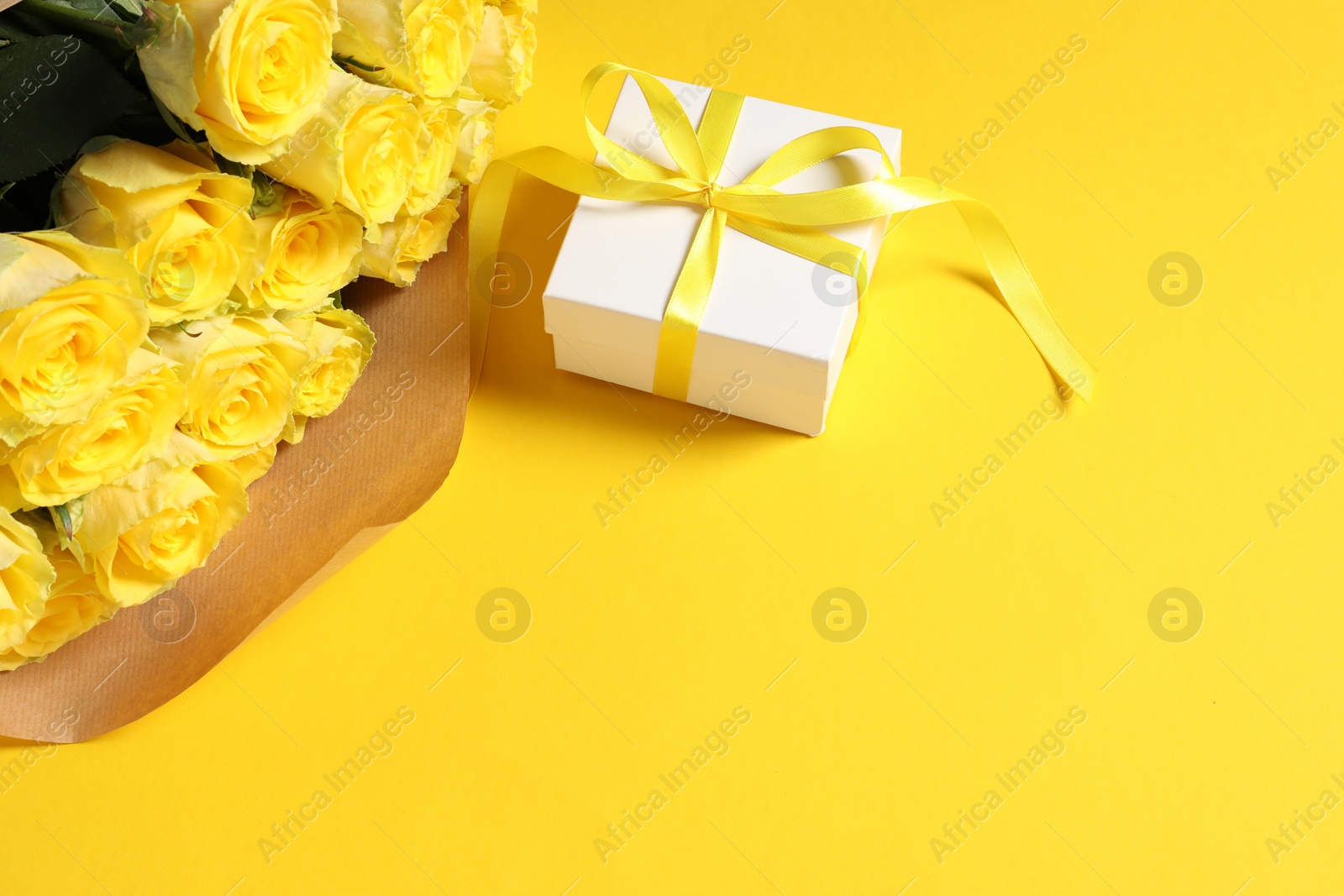 Photo of Beautiful bouquet of roses and gift box on yellow background, above view. Space for text