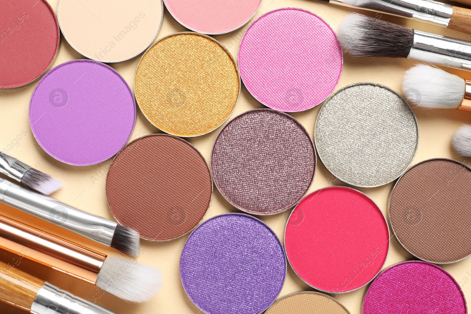 Photo of Different beautiful eye shadows and makeup brushes on beige background, flat lay