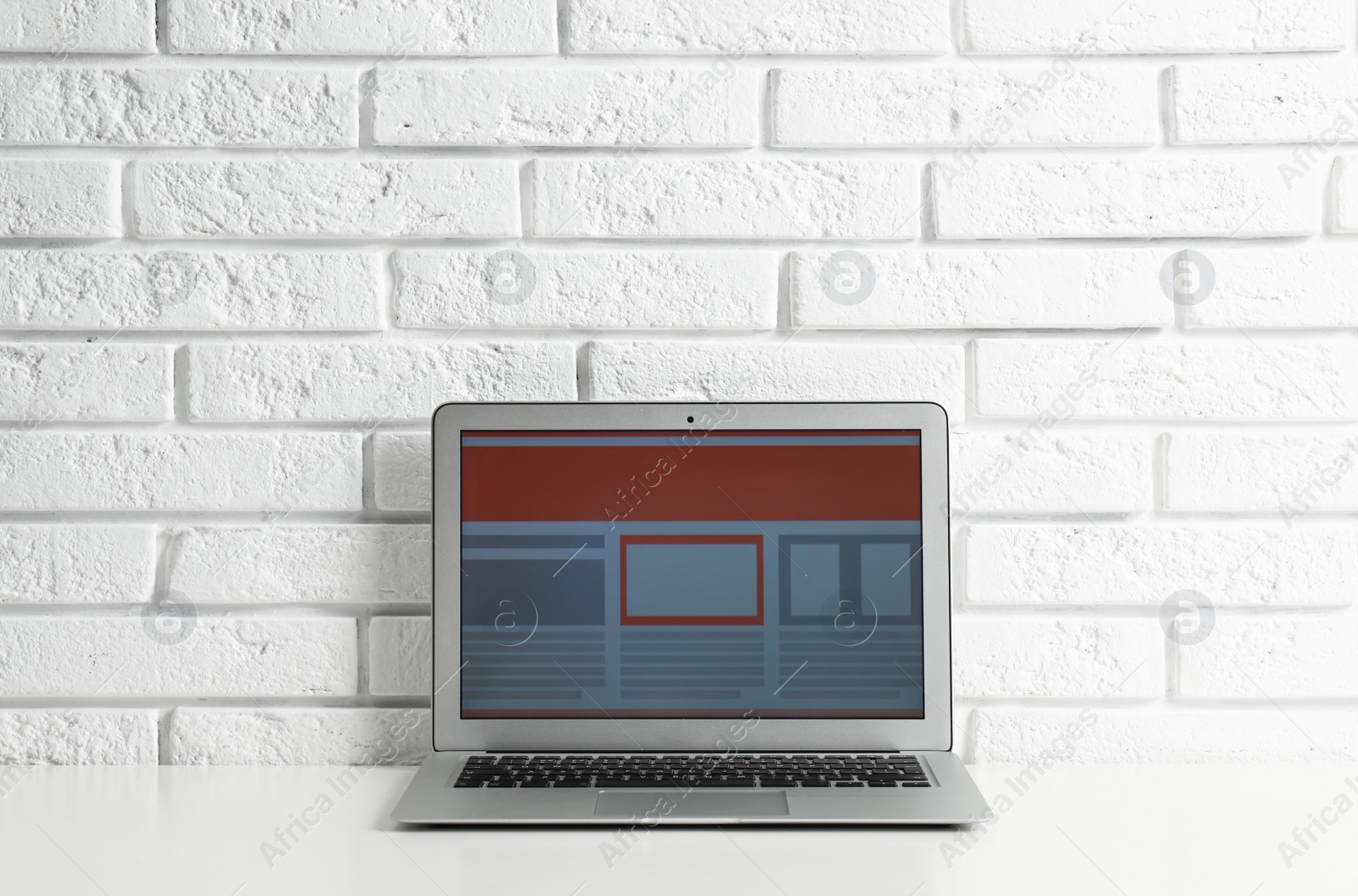 Photo of Modern workplace with laptop on table near brick wall. Space for design