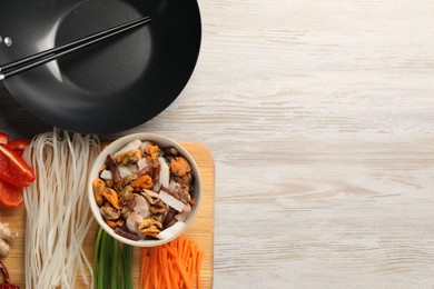 Photo of Black wok, chopsticks and board with products on light wooden table, top view. Space for text