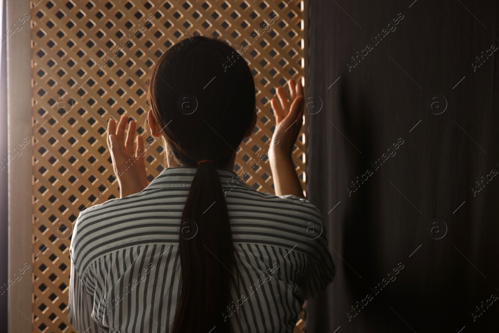 Photo of Woman praying to God during confession in booth, back view