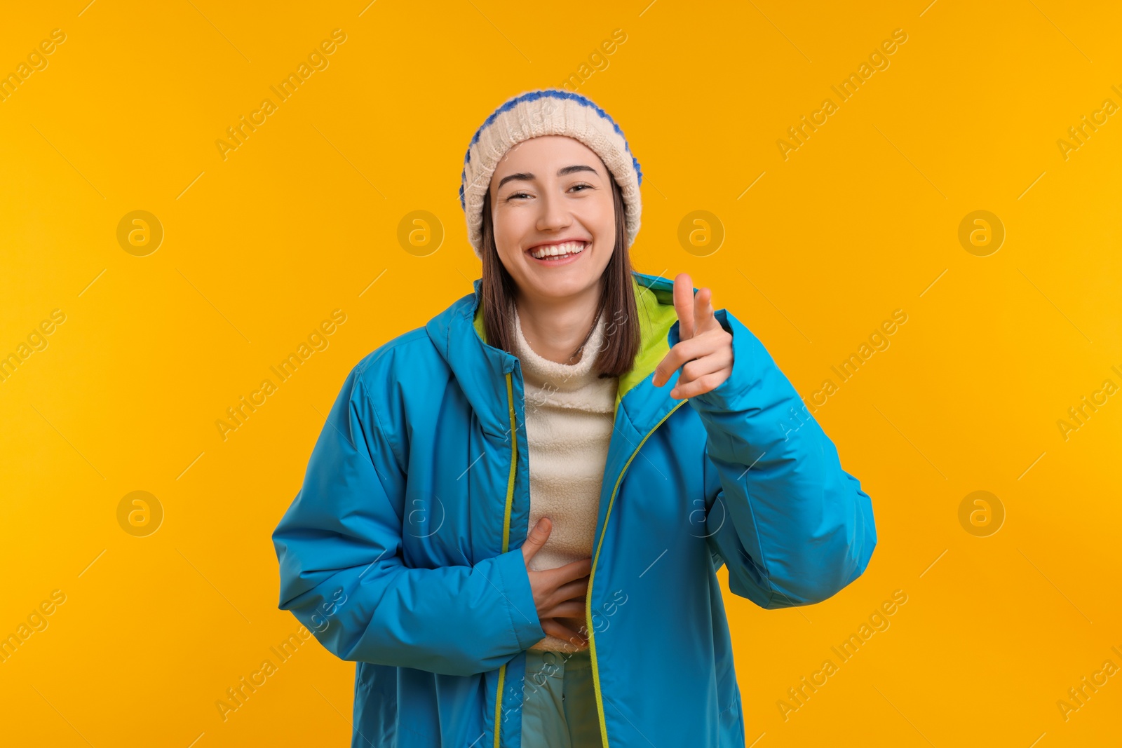 Photo of Portrait of beautiful woman laughing and pointing at something on orange background