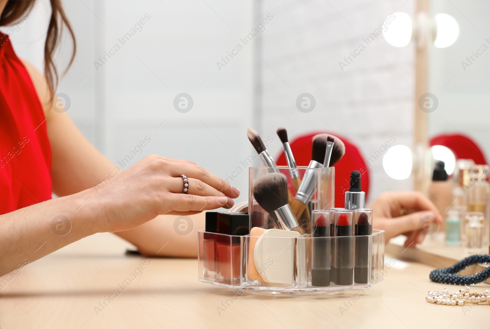 Photo of Woman reaching for organizer with cosmetic products and makeup accessories on dressing table indoors, closeup