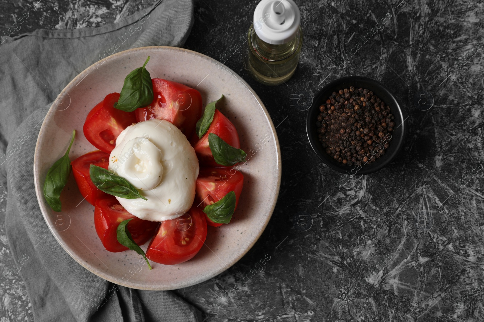 Photo of Delicious burrata cheese with tomatoes and basil, oil and peppercorns on grey table, flat lay