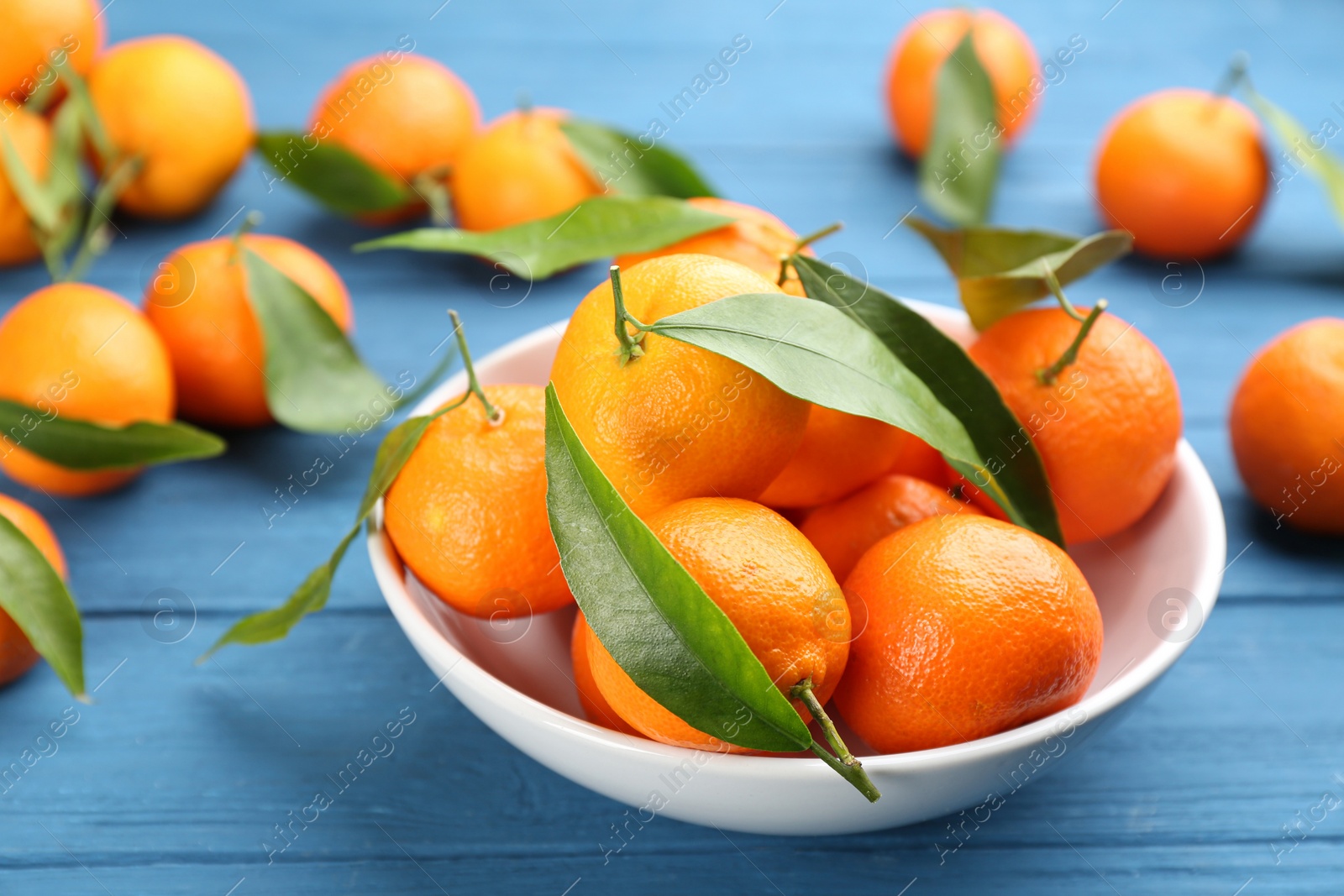 Photo of Fresh ripe tangerines with green leaves on blue wooden table, closeup
