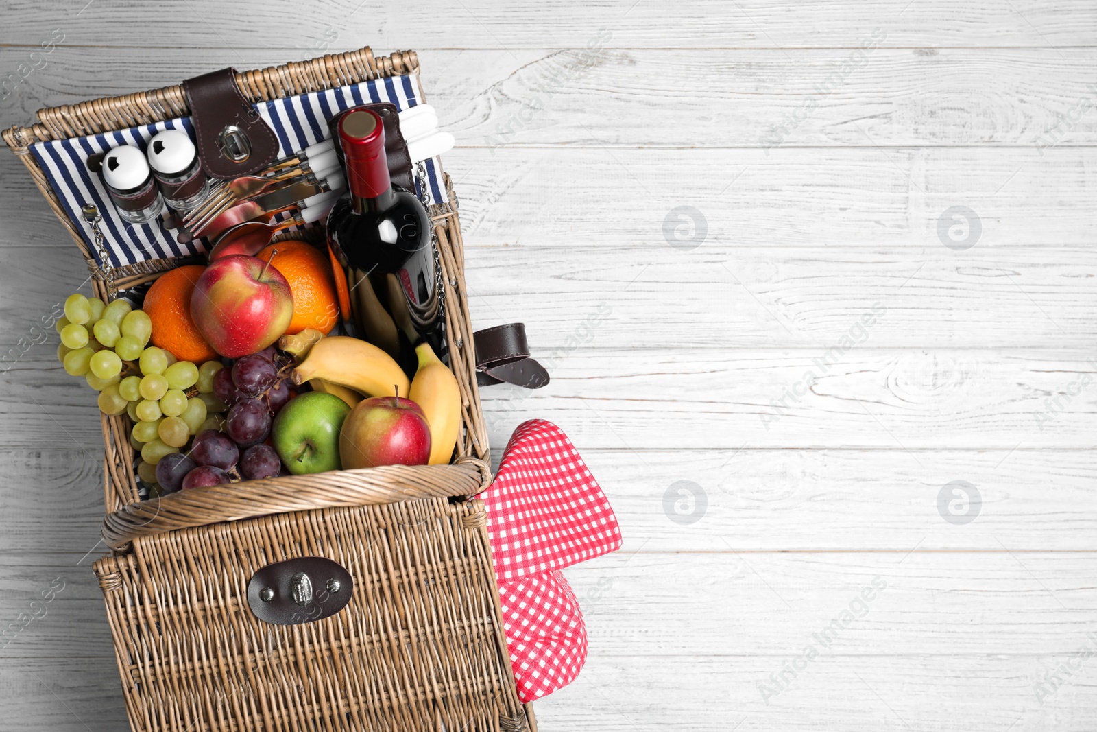 Photo of Wicker picnic basket with wine and different products on wooden table, top view. Space for text