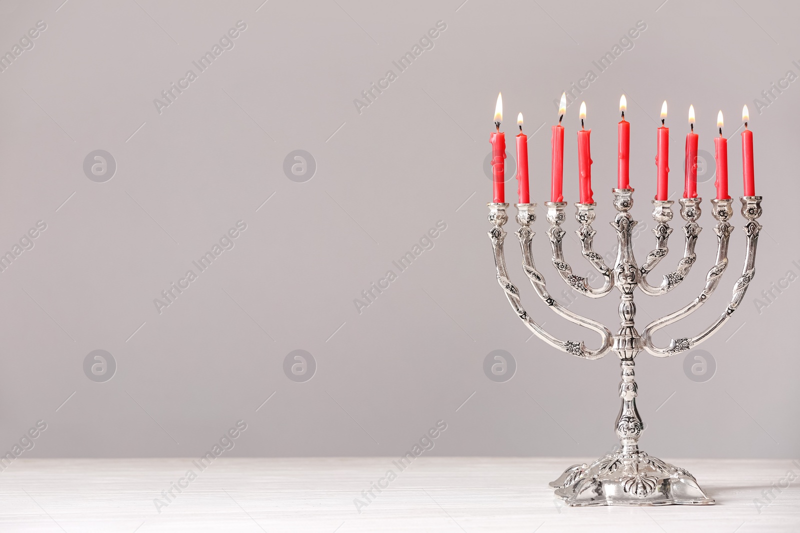 Photo of Silver menorah with burning candles on table against light grey background. Hanukkah celebration