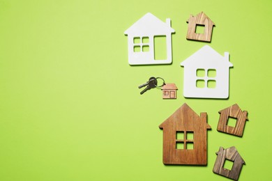 Photo of House models and keys on light green background, flat lay. Space for text