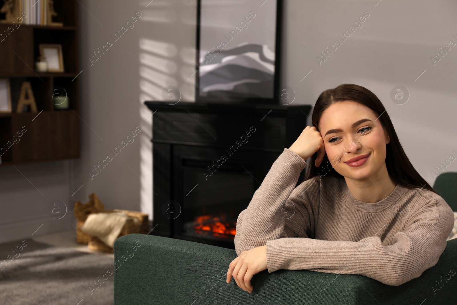 Photo of Beautiful young woman sitting on sofa near fireplace in living room. Space for text