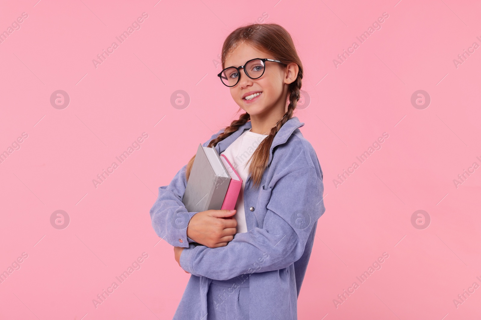 Photo of Smiling schoolgirl with books on pink background