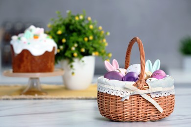 Photo of Easter basket with painted eggs and decorations on white marble table. Space for text