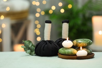 Photo of Spa composition. Herbal massage bags, stones and burning candles on white towel against blurred lights