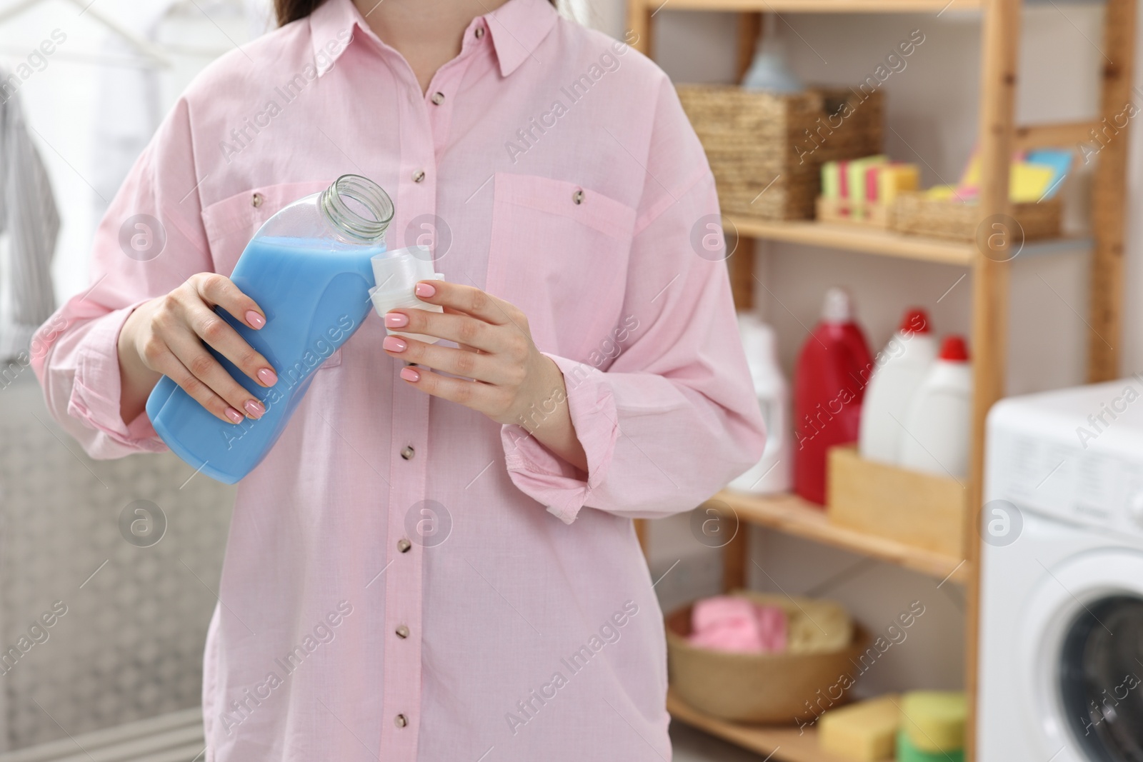 Photo of Woman pouring detergent into cap in laundry room, closeup