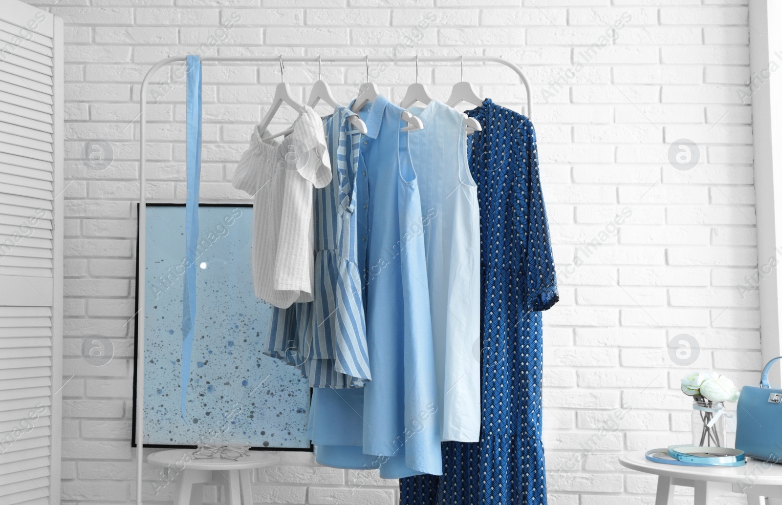 Photo of Wardrobe rack with women's clothes at white brick wall in room