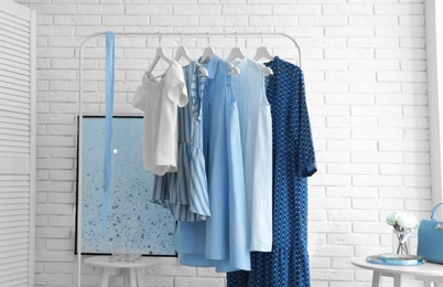 Photo of Wardrobe rack with women's clothes at white brick wall in room