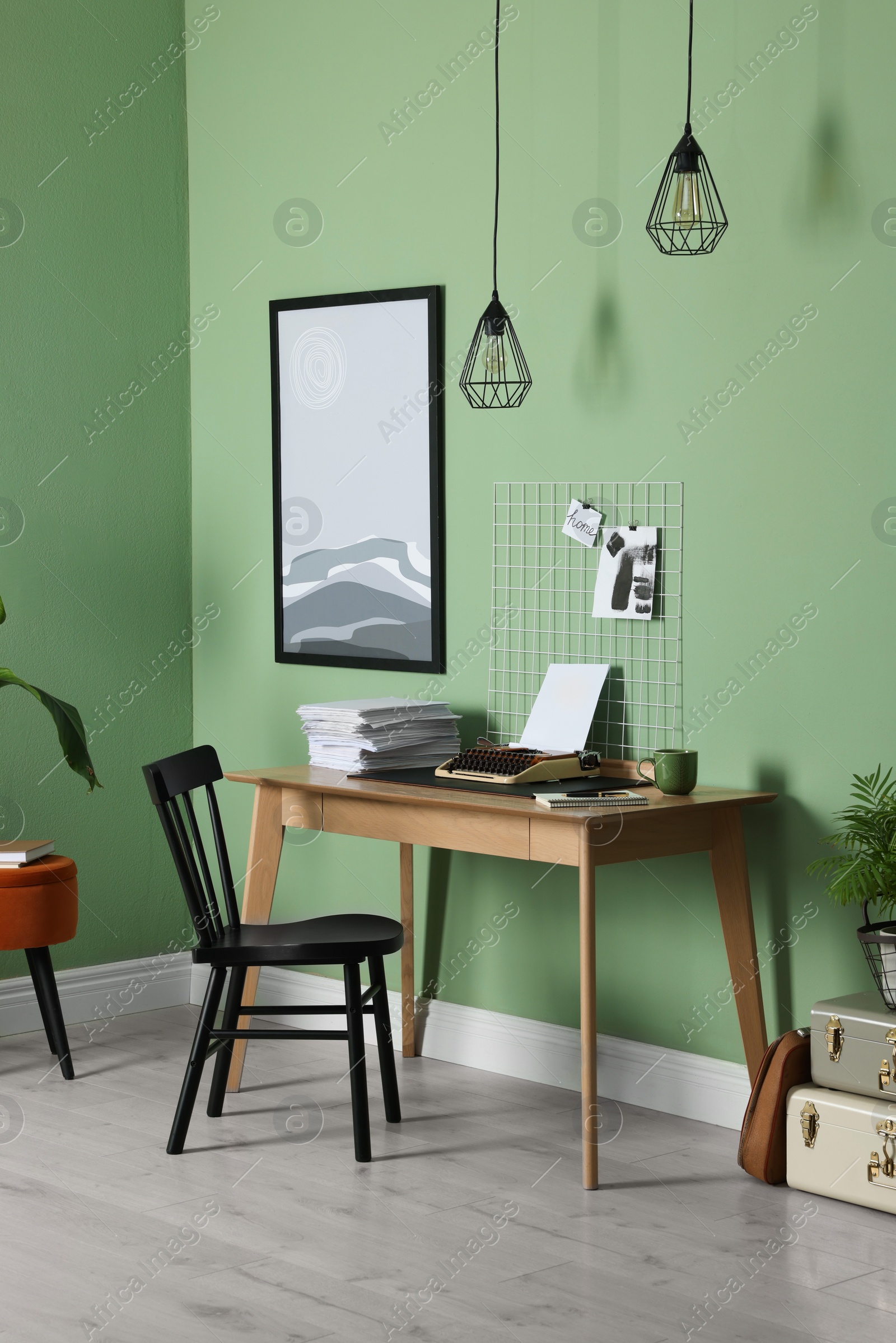 Photo of Typewriter, stack of papers and mood board on wooden table near pale green wall. Writer's workplace