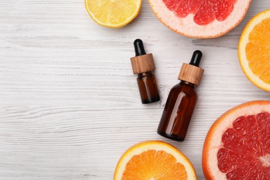 Photo of Bottles of citrus essential oils and fresh fruit slices on white wooden table, flat lay. Space for text