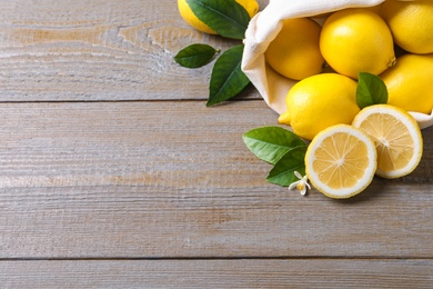 Many fresh ripe lemons with green leaves and flower on wooden table. Space for text