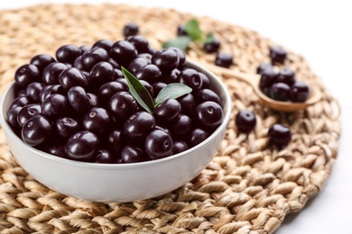 Tasty acai berries in bowl on wicker mat, closeup