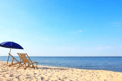 Empty wooden sunbeds and umbrella on sandy shore. Beach accessories