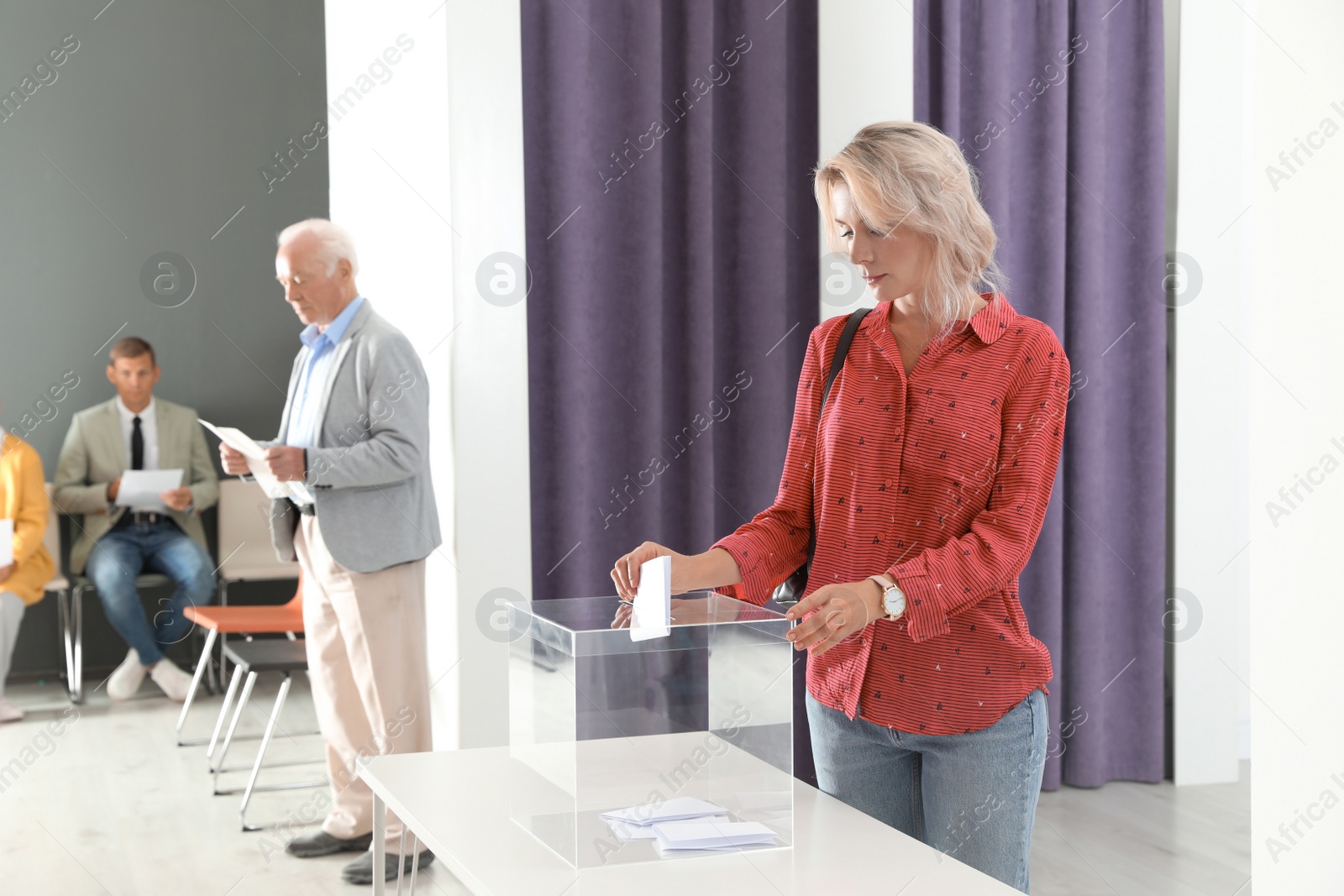 Photo of Woman putting her vote into ballot box on table indoors