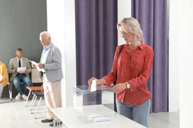 Photo of Woman putting her vote into ballot box on table indoors