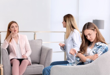 Photo of Young female psychologist working with teenage girl and her mother in office