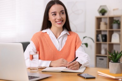 Photo of Young woman writing in notebook at wooden table indoors