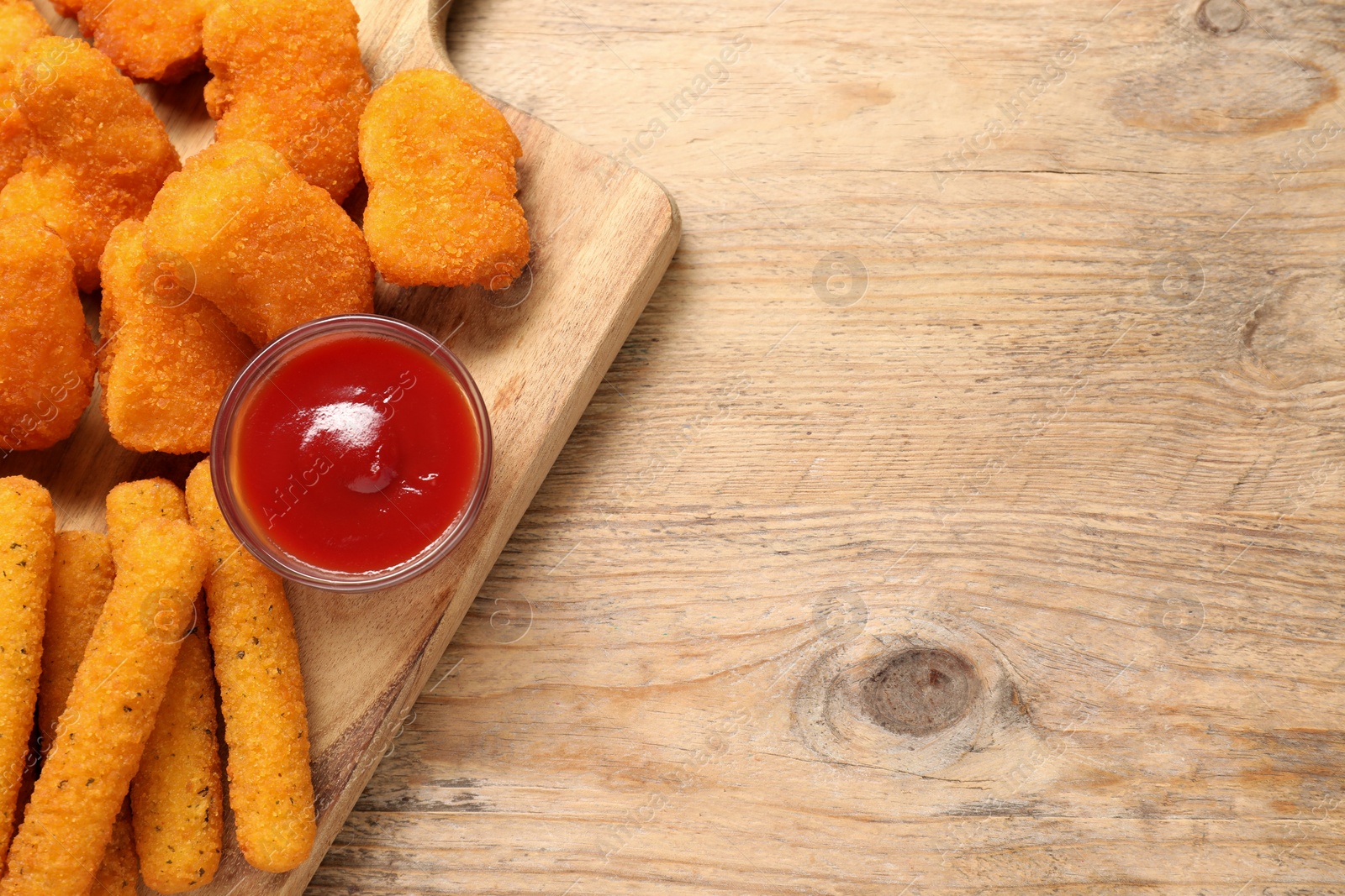 Photo of Board with tasty ketchup, cheese sticks and chicken nuggets on wooden table, top view. Space for text