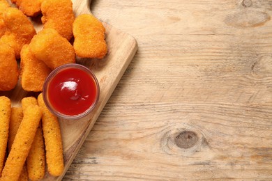 Board with tasty ketchup, cheese sticks and chicken nuggets on wooden table, top view. Space for text