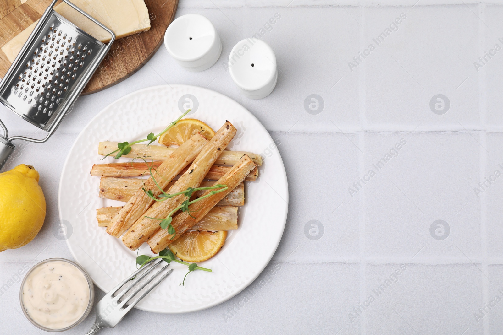 Photo of Plate with baked salsify roots, lemon, fork and sauce on white tiled table, flat lay. Space for text