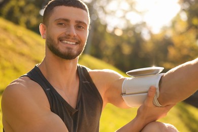 Attractive happy man checking blood pressure with modern monitor after training on sunny day
