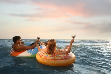 Couple with glasses of wine and inflatable rings in sea