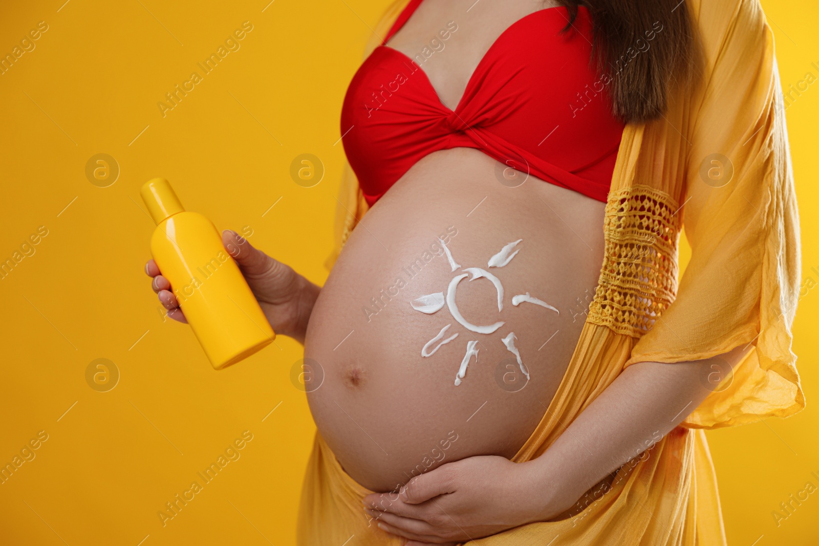 Photo of Young pregnant woman with sun protection cream on yellow background, closeup