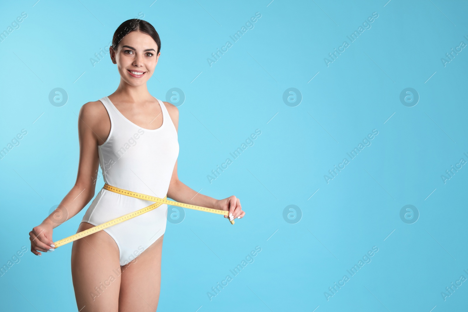 Photo of Attractive young woman with slim body measuring her waist on color background. Space for text